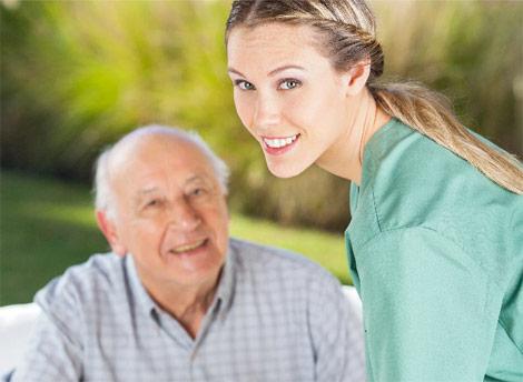 Female caregiver smiling beside senior man providing compassionate senior care outdoors